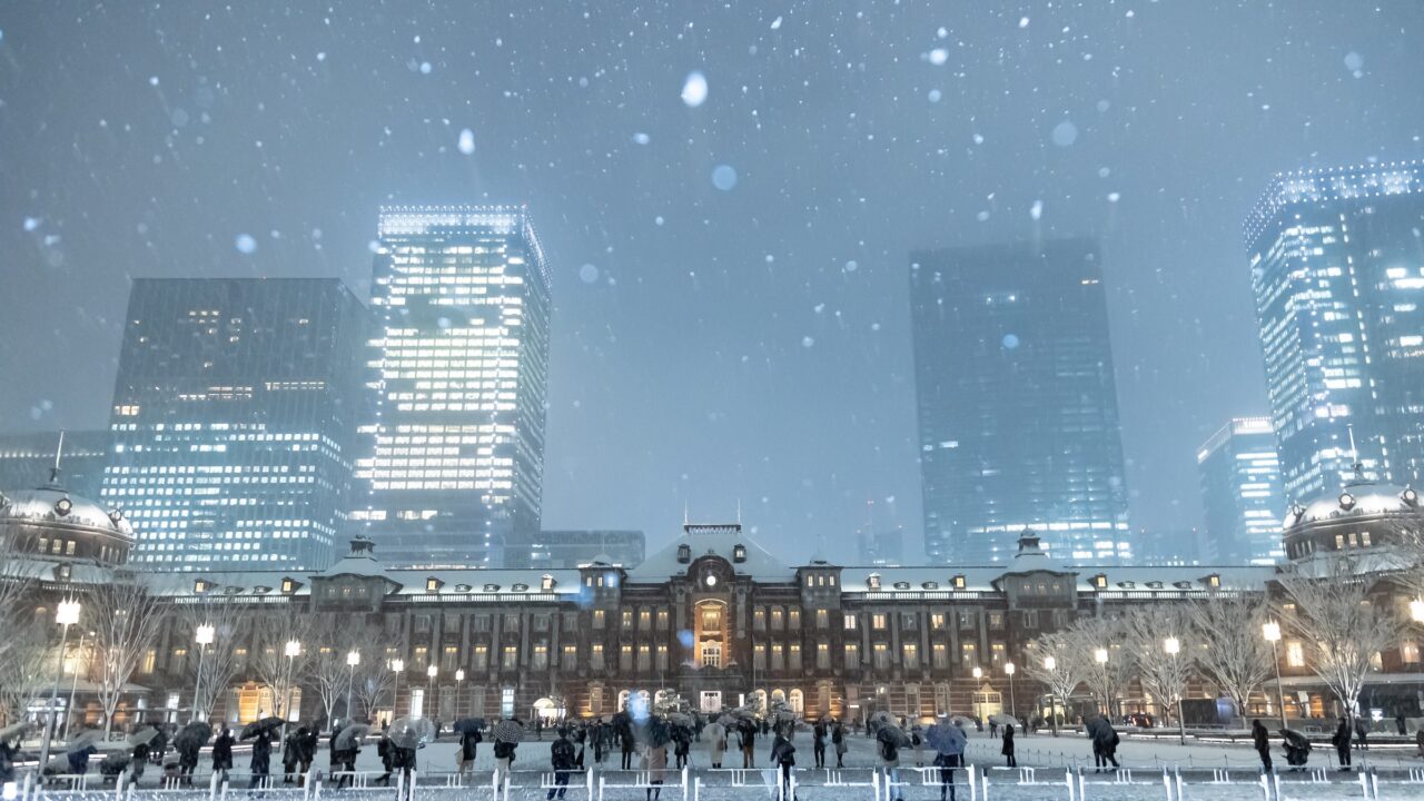 Snow falling at night in front of a floodlit brick station building