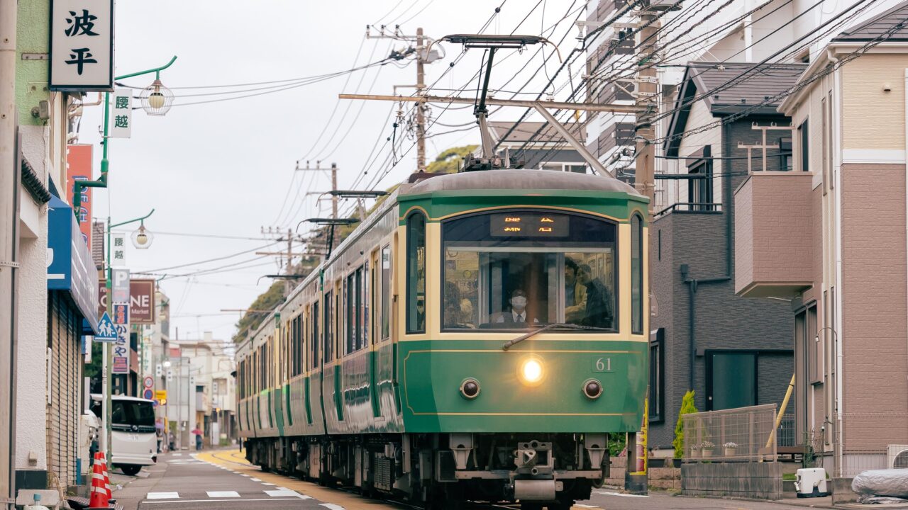 A green and cream tram running down the middle of a narrow residential street