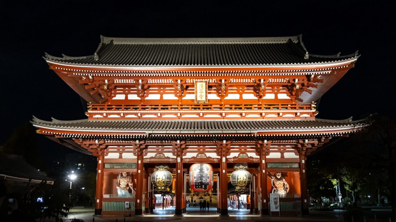 A two-storey temple gate lit from within at night, hung with lanterns