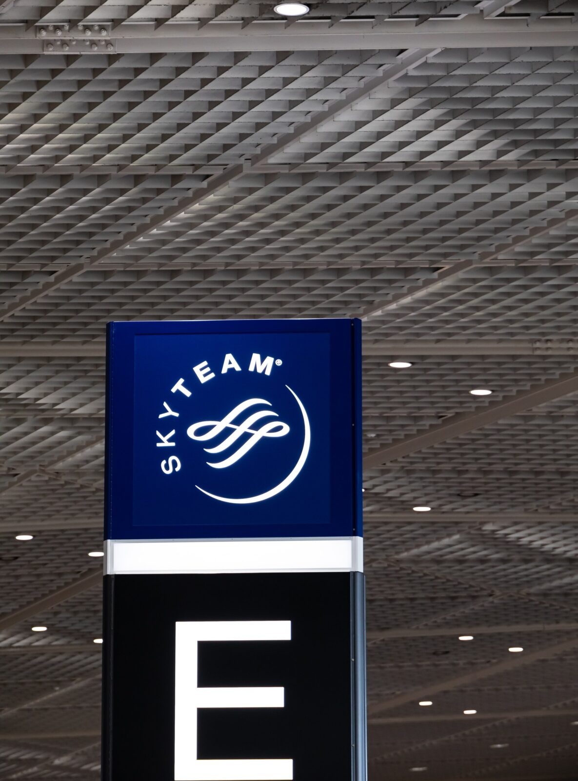 An illuminated terminal sign showing the letter E above an airport concourse