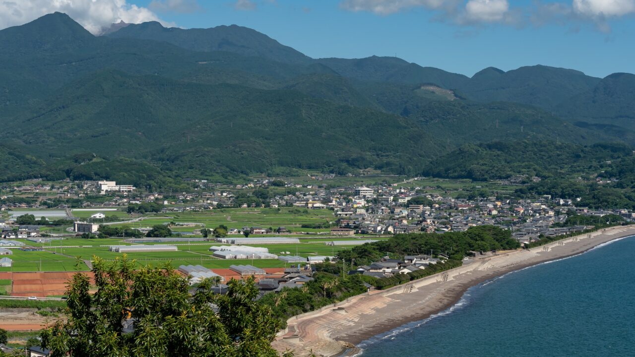 A small coastal town below wooded hills, seen from above