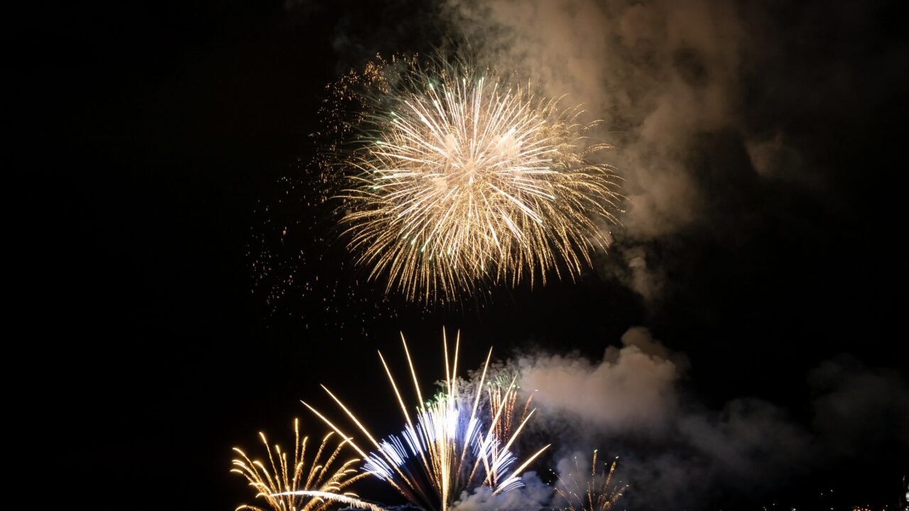 Several fireworks bursting low over water in smoke