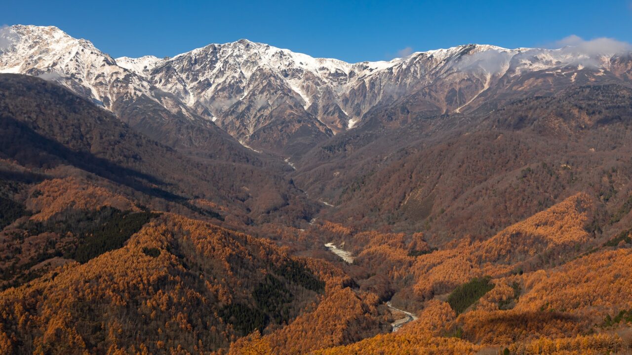 A deep valley of autumn forest below a high snow-covered ridge
