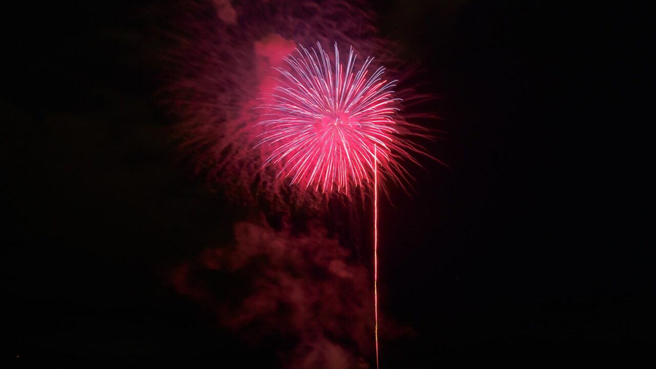 A red firework opening high above a dark shoreline