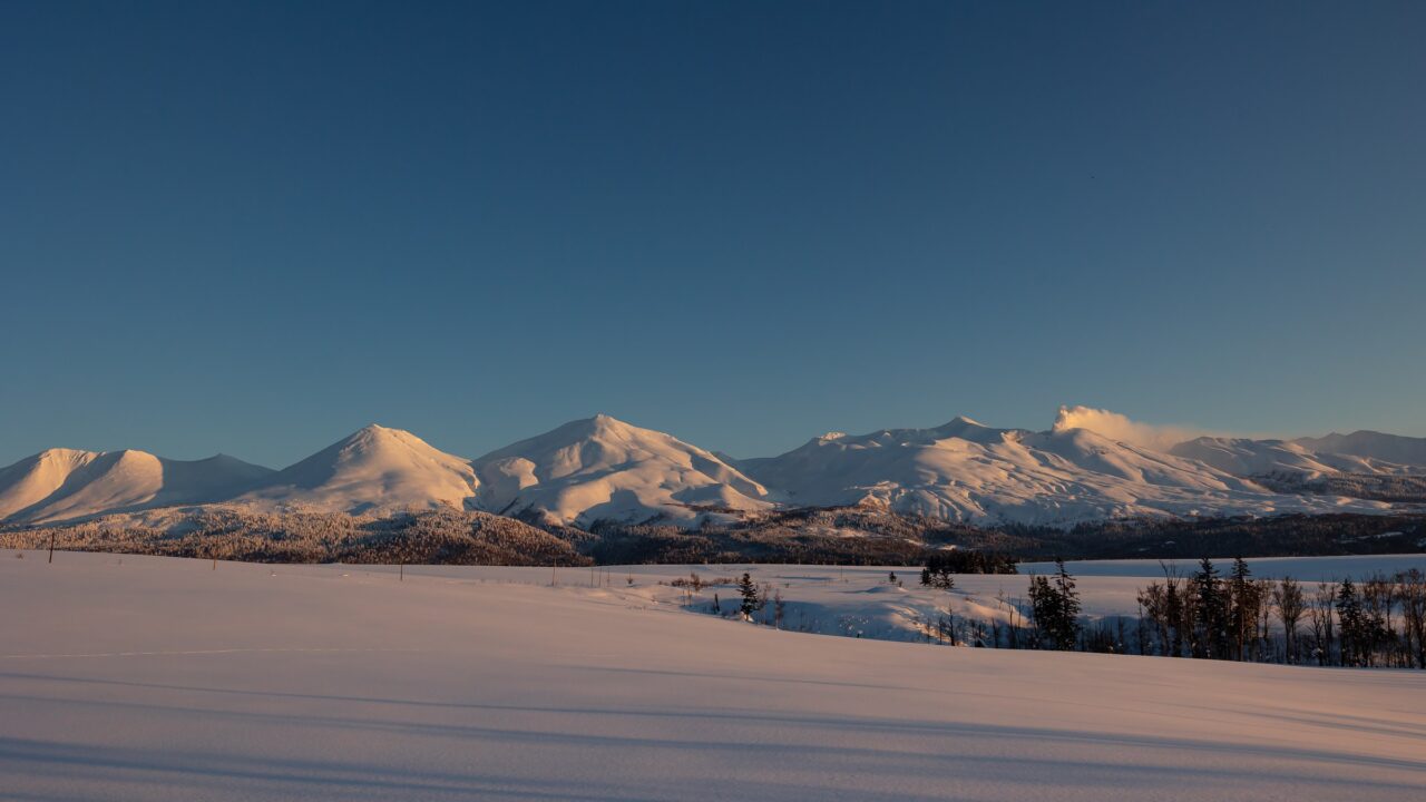 A long range of snow-covered peaks above a flat snow-covered plain