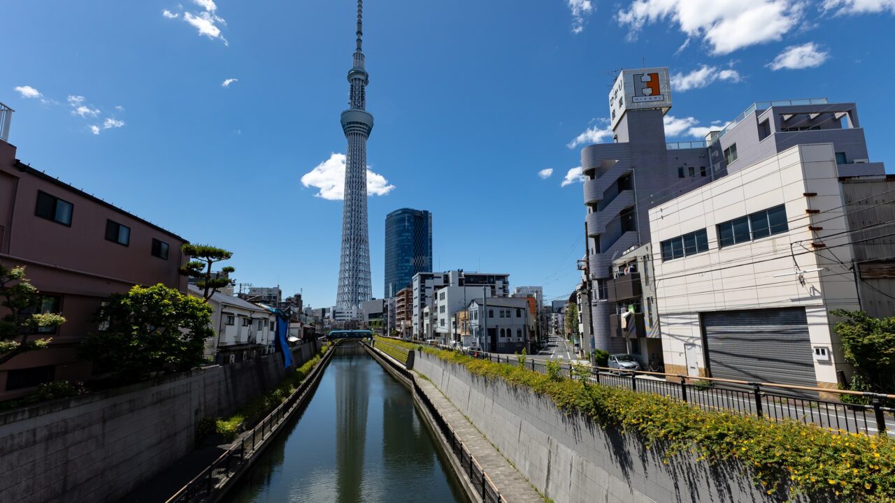 A canal running between low buildings with a tall broadcasting tower beyond